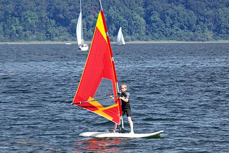 Kind am Windsurfen mit rotem Segel